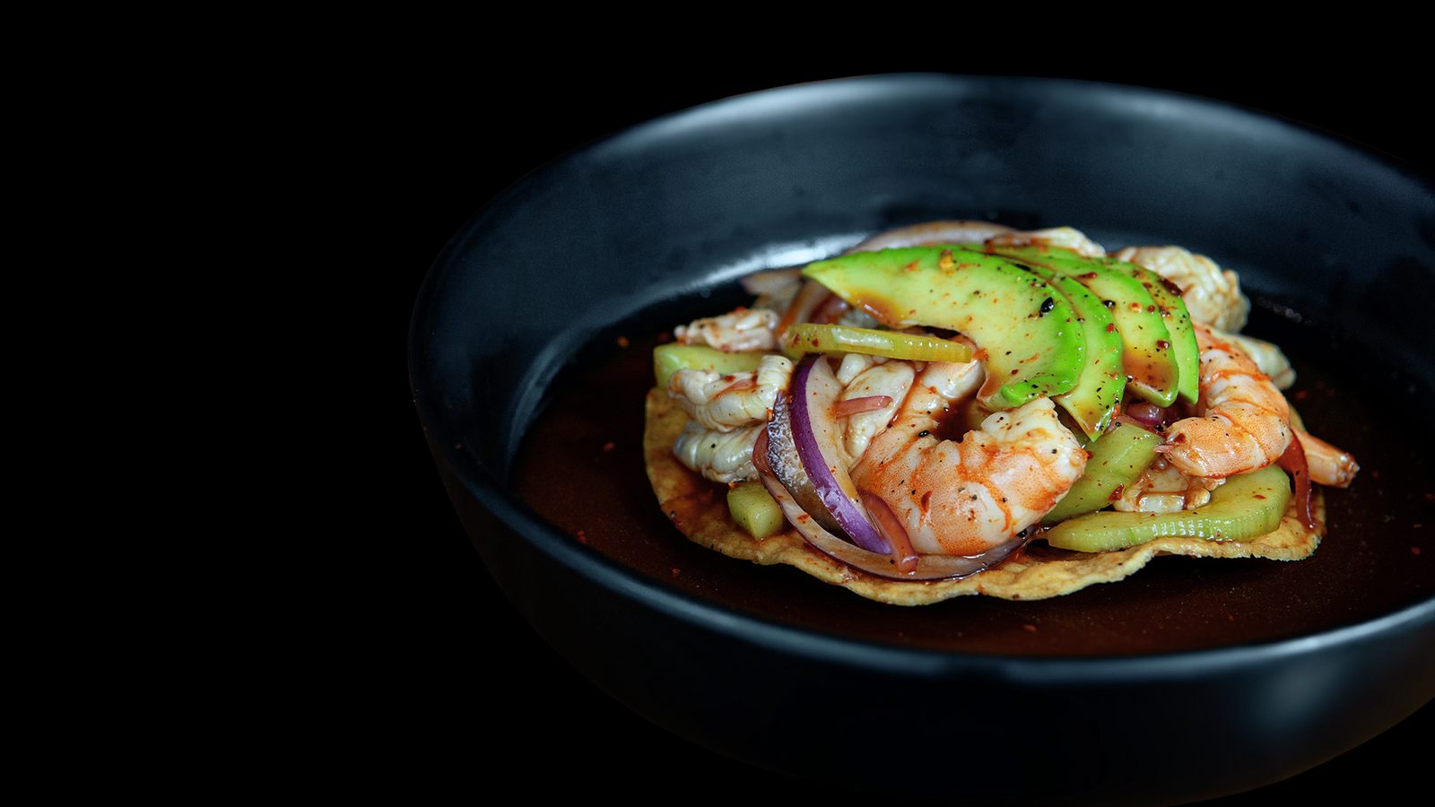 Tostada especial de camarón y pulpo con aguacate, servida en plato negro